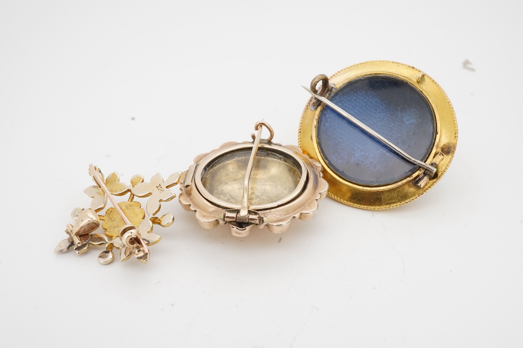Three brooches, comprising: a Victorian circular brooch centring on a cabochon onyx set with a rose-cut diamond in a star setting, to concentring bands of seed pearls and Greek key motifs in black enamel, the reverse wit